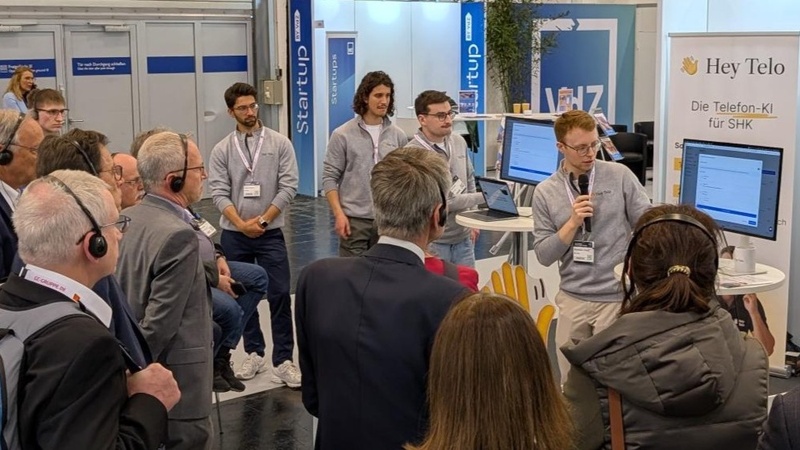Teilnehmer eines Messerundgangs verfolgen eine Präsentation am Stand von Hey Telo.